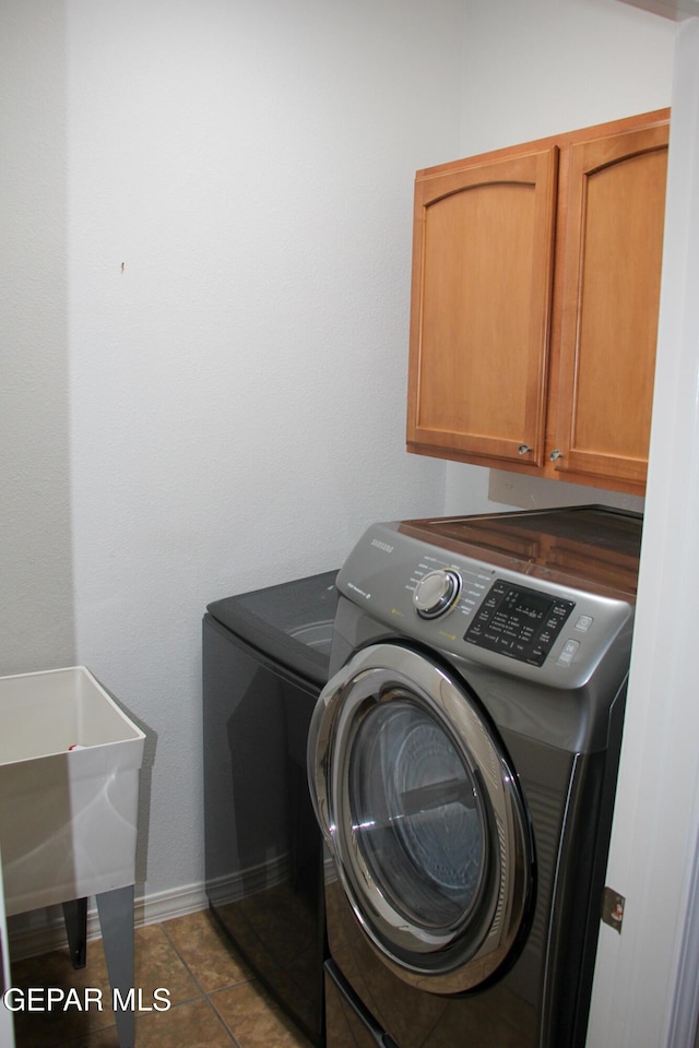 laundry room with washing machine and clothes dryer, tile patterned floors, and cabinets