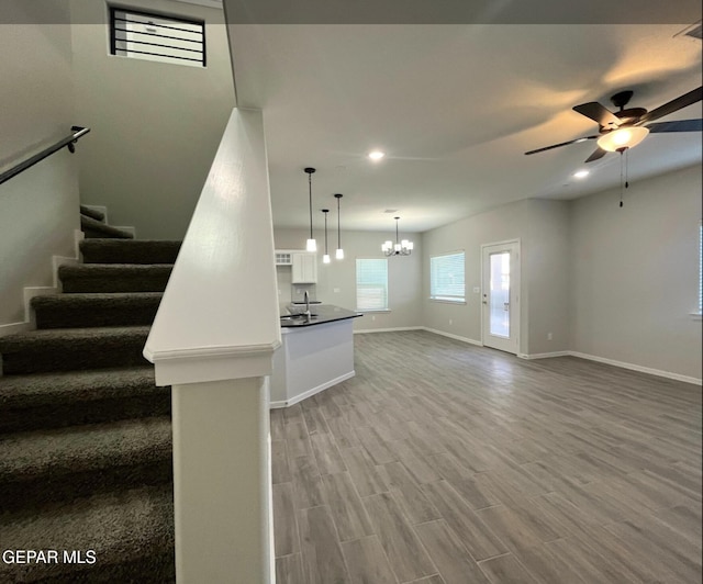 unfurnished living room featuring hardwood / wood-style flooring, ceiling fan with notable chandelier, and sink