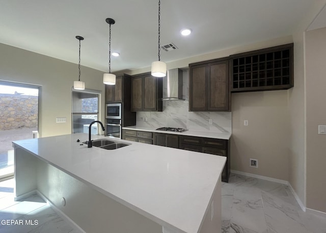 kitchen featuring backsplash, a kitchen island with sink, wall chimney range hood, hanging light fixtures, and appliances with stainless steel finishes