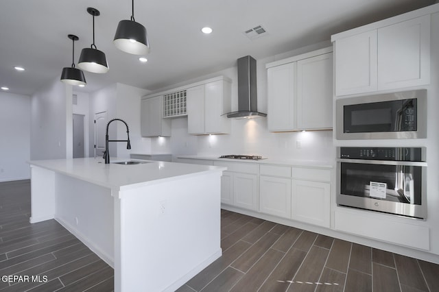 kitchen with wall chimney range hood, a sink, built in microwave, stainless steel oven, and wood finish floors