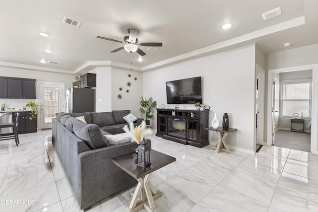 living room featuring ceiling fan, a raised ceiling, and a fireplace