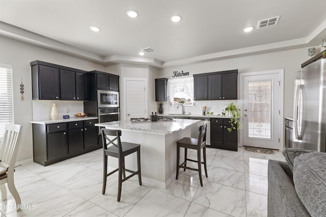 kitchen with a wealth of natural light, a center island, a breakfast bar area, and appliances with stainless steel finishes