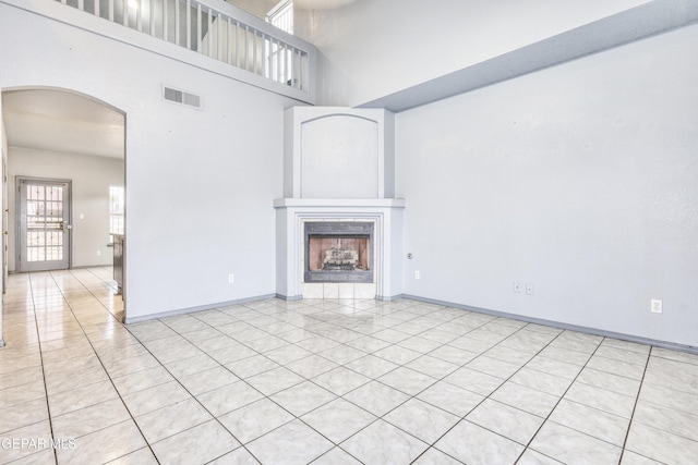 unfurnished living room featuring a tiled fireplace, a towering ceiling, and light tile patterned flooring