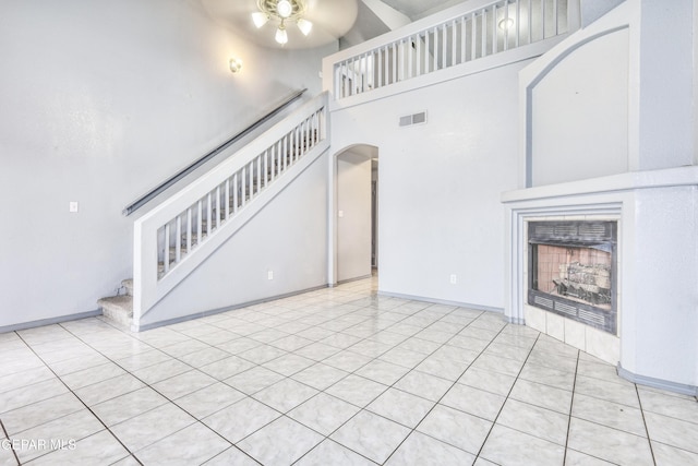 unfurnished living room featuring a fireplace, light tile patterned floors, a towering ceiling, and ceiling fan