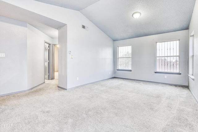 unfurnished room with lofted ceiling, a textured ceiling, and light carpet