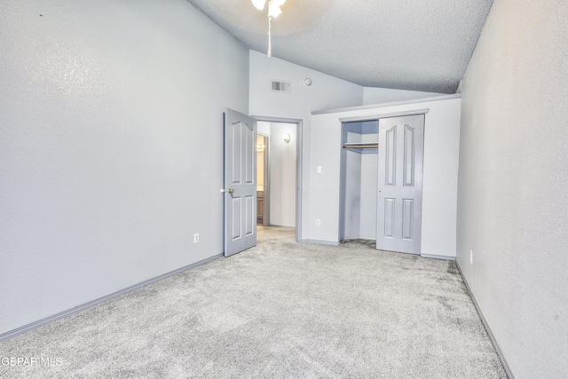 unfurnished bedroom featuring a closet, light colored carpet, a textured ceiling, and vaulted ceiling