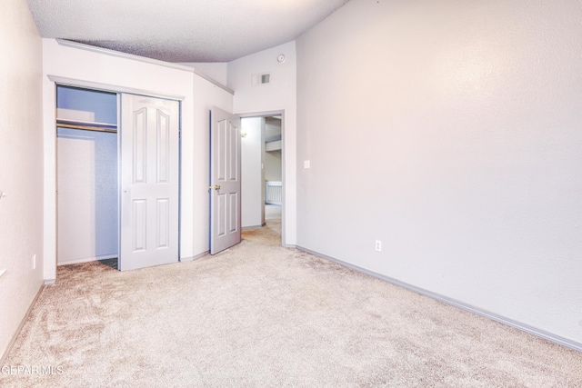 unfurnished bedroom with a textured ceiling, light colored carpet, vaulted ceiling, and a closet