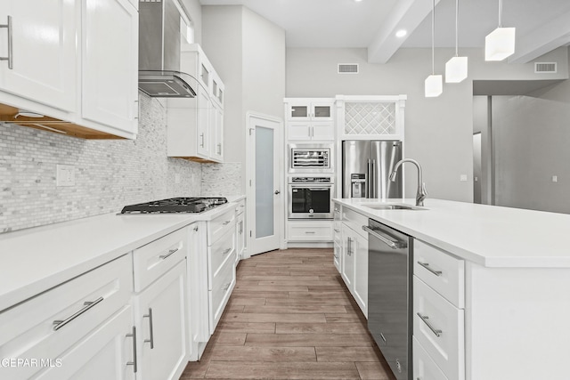 kitchen with white cabinets, sink, wall chimney exhaust hood, appliances with stainless steel finishes, and beamed ceiling