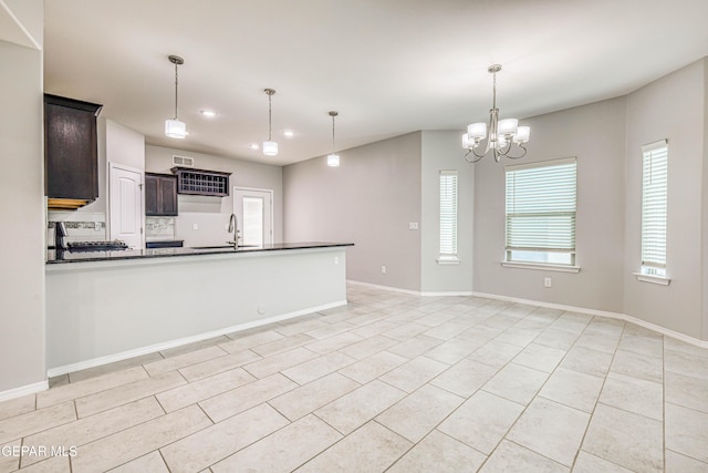 kitchen with dark brown cabinetry, sink, a healthy amount of sunlight, and an inviting chandelier