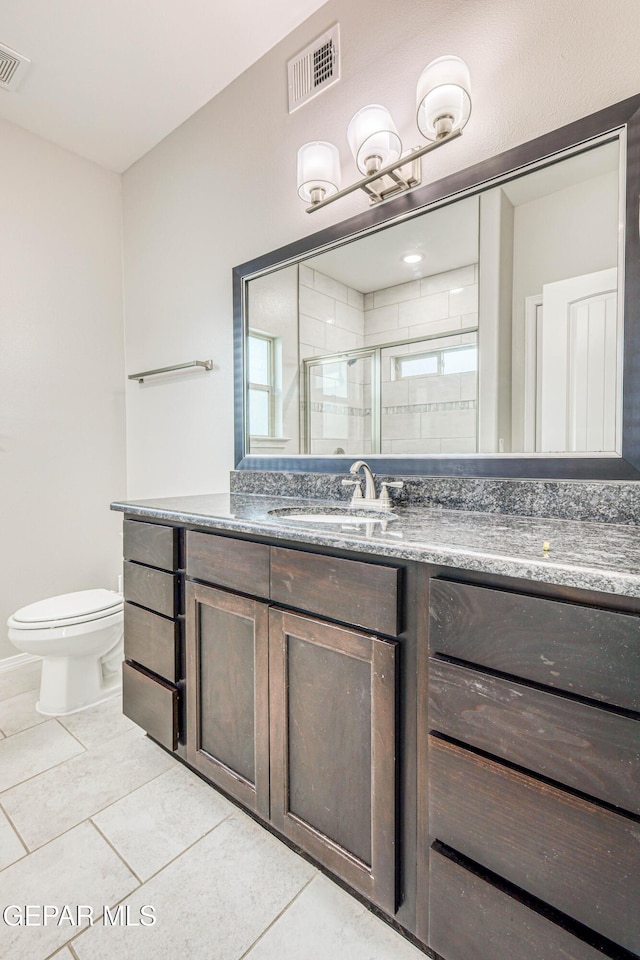 bathroom featuring tile patterned flooring, vanity, a shower with shower door, and toilet