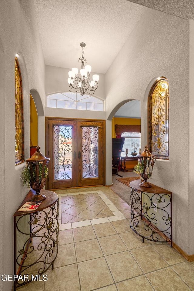 foyer entrance featuring a high ceiling, a textured ceiling, light tile patterned floors, and a notable chandelier