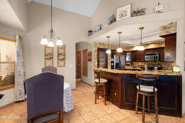 kitchen with dark brown cabinets, hanging light fixtures, tasteful backsplash, a breakfast bar area, and stainless steel appliances