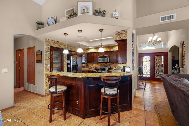 kitchen featuring stainless steel appliances, a kitchen bar, a towering ceiling, and decorative light fixtures