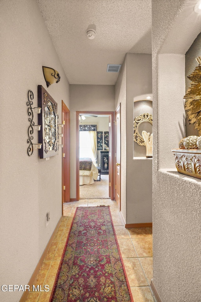 hallway with a textured ceiling and light tile patterned floors