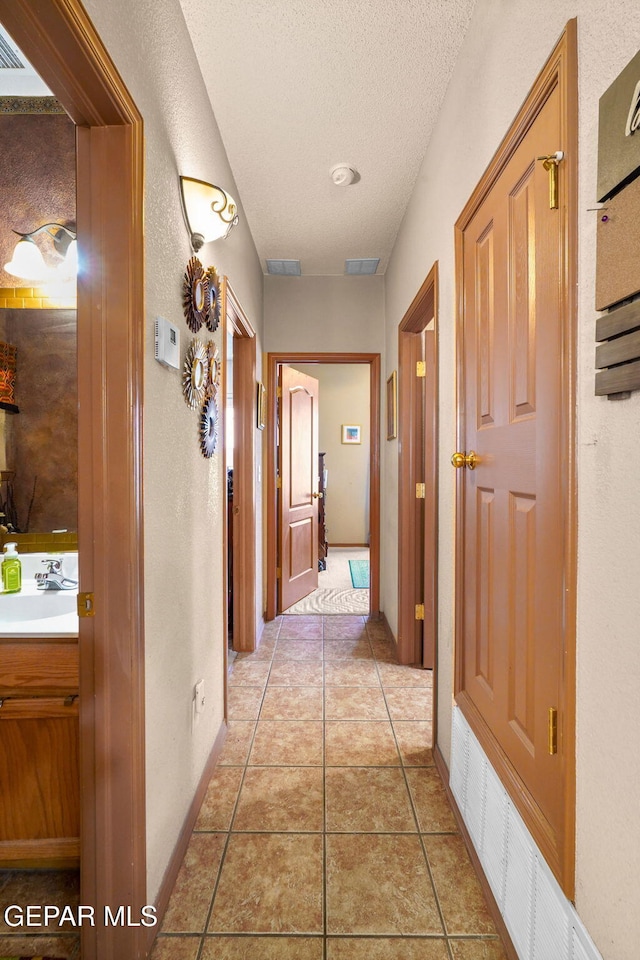 corridor with sink, a textured ceiling, and tile patterned flooring