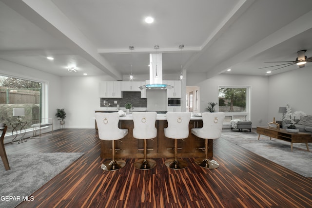 kitchen with ceiling fan, hanging light fixtures, white cabinets, a kitchen bar, and beamed ceiling