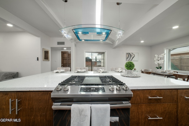 kitchen featuring a kitchen island, island range hood, decorative light fixtures, stainless steel gas stove, and a healthy amount of sunlight