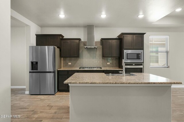 kitchen with a center island with sink, dark brown cabinets, wall chimney range hood, and stainless steel appliances