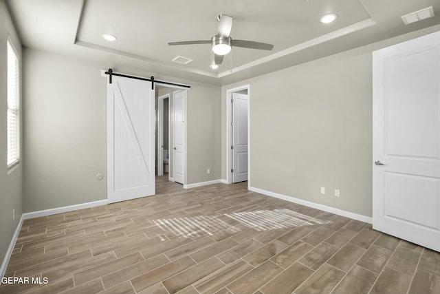 unfurnished bedroom with multiple windows, a barn door, a raised ceiling, and ceiling fan