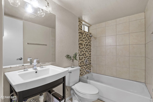 full bathroom with sink, tiled shower / bath combo, a textured ceiling, and toilet