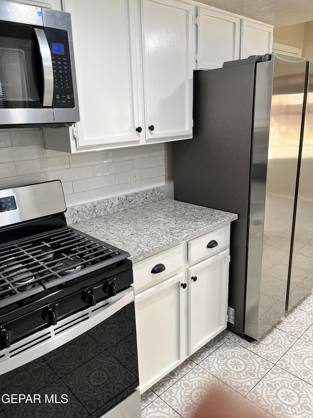 kitchen with backsplash, light stone countertops, light tile patterned floors, appliances with stainless steel finishes, and white cabinetry