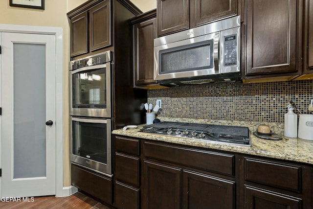 kitchen with dark brown cabinetry, stainless steel appliances, tasteful backsplash, light stone counters, and dark hardwood / wood-style floors