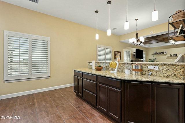 kitchen with pendant lighting, a notable chandelier, light stone counters, and dark brown cabinetry