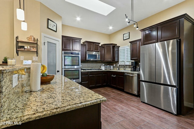 kitchen featuring light stone countertops, appliances with stainless steel finishes, a skylight, dark brown cabinets, and decorative light fixtures