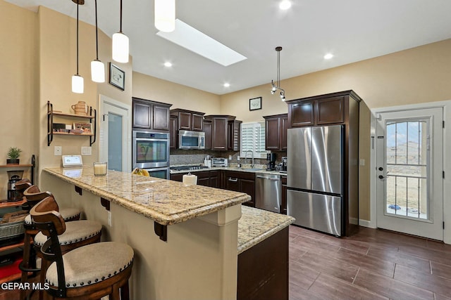 kitchen featuring a skylight, light stone counters, kitchen peninsula, pendant lighting, and appliances with stainless steel finishes