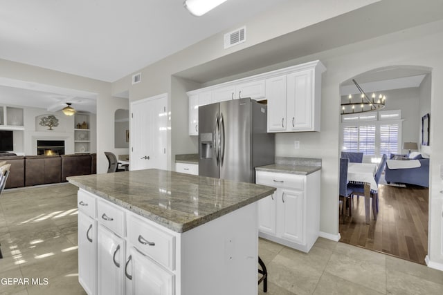 kitchen with stainless steel fridge, built in features, dark stone countertops, a center island, and white cabinetry