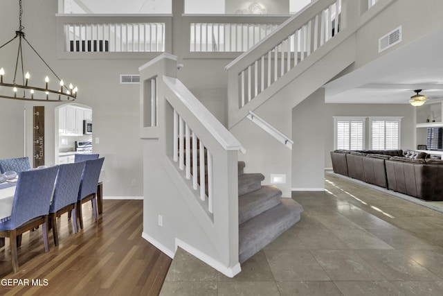 staircase featuring a high ceiling and ceiling fan with notable chandelier