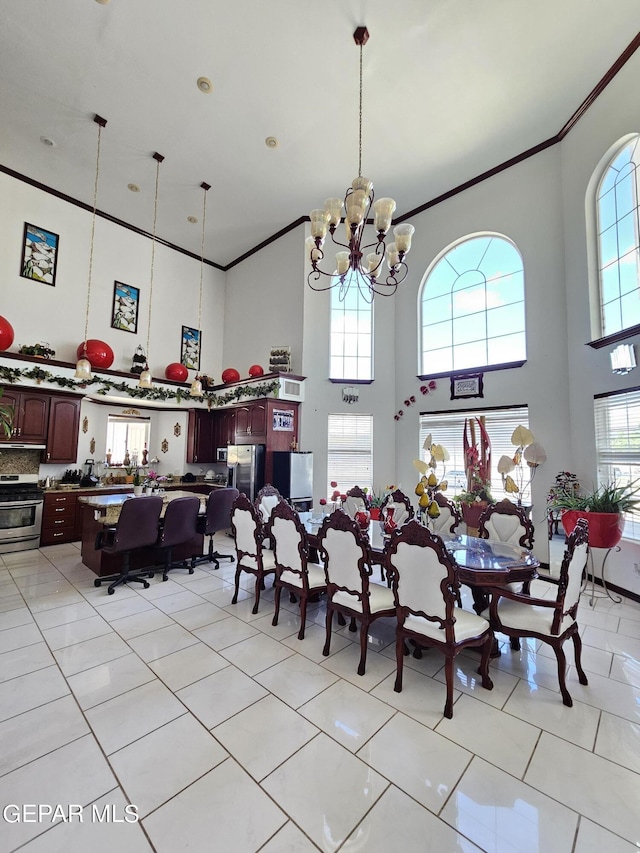 tiled dining area with a high ceiling, an inviting chandelier, plenty of natural light, and ornamental molding