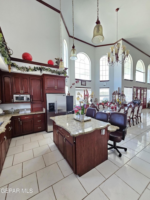 kitchen with light stone countertops, stainless steel refrigerator with ice dispenser, a towering ceiling, decorative light fixtures, and an inviting chandelier