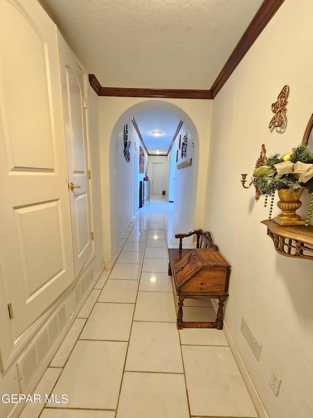 corridor featuring a textured ceiling, light tile patterned flooring, and crown molding