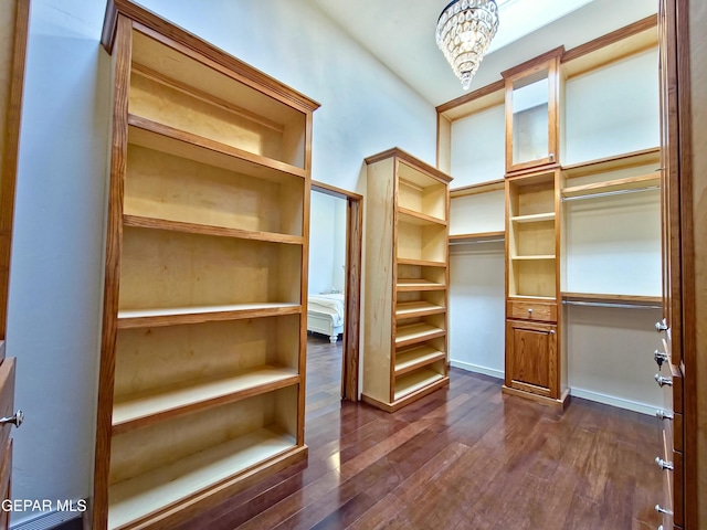 walk in closet with a notable chandelier and dark wood-type flooring