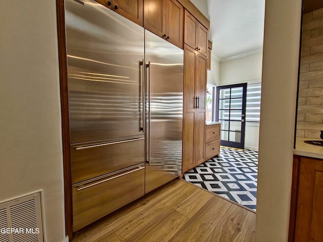 kitchen featuring stainless steel built in refrigerator, light hardwood / wood-style floors, and ornamental molding