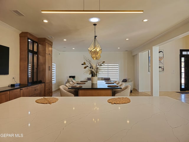 kitchen featuring pendant lighting, light hardwood / wood-style flooring, ornamental molding, and dark stone countertops