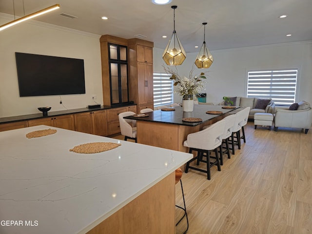 kitchen with pendant lighting, dark stone counters, crown molding, light wood-type flooring, and a breakfast bar area