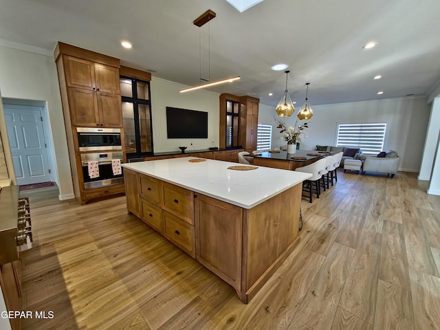 kitchen featuring a large island, stainless steel double oven, hanging light fixtures, crown molding, and light wood-type flooring