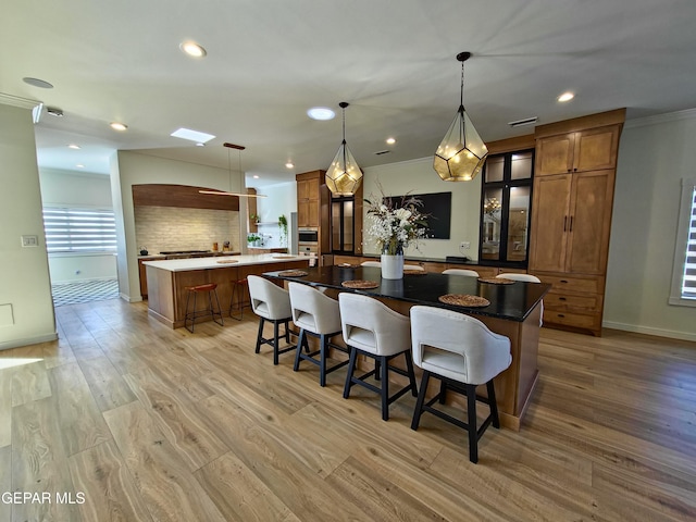 kitchen with backsplash, decorative light fixtures, light hardwood / wood-style flooring, and a spacious island