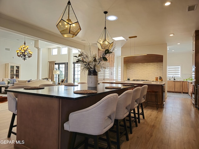 kitchen featuring a kitchen breakfast bar, ornate columns, decorative backsplash, and hanging light fixtures