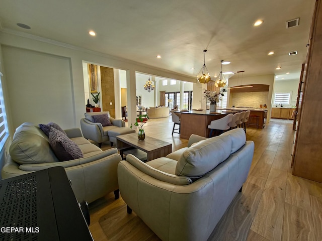 living room with ornamental molding, light hardwood / wood-style flooring, a wealth of natural light, and a notable chandelier