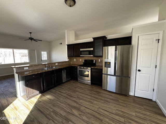 kitchen featuring stainless steel appliances, dark stone counters, ceiling fan, sink, and backsplash