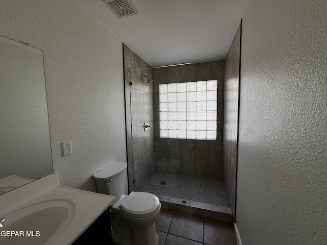 bathroom featuring tiled shower, tile patterned flooring, vanity, and toilet