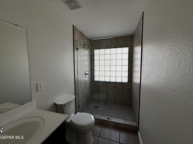 bathroom with a tile shower, tile patterned flooring, vanity, and toilet