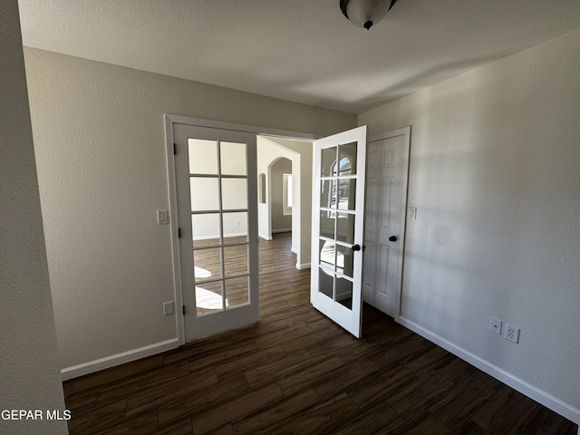 empty room with a textured ceiling, dark hardwood / wood-style flooring, and french doors