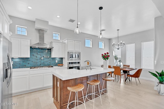 kitchen featuring white cabinetry, backsplash, pendant lighting, a kitchen island with sink, and appliances with stainless steel finishes