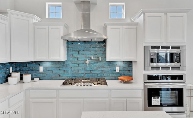 kitchen with white cabinetry, wall chimney exhaust hood, a healthy amount of sunlight, and appliances with stainless steel finishes