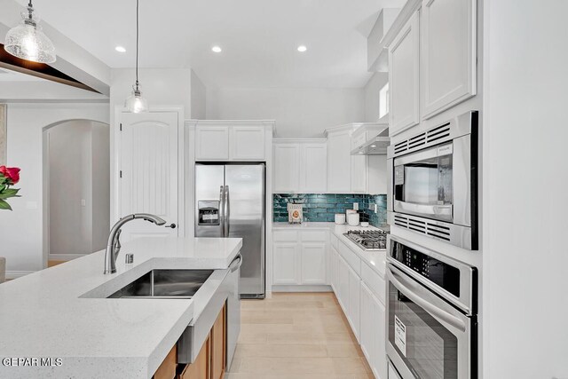 kitchen featuring appliances with stainless steel finishes, tasteful backsplash, a kitchen island with sink, decorative light fixtures, and white cabinetry