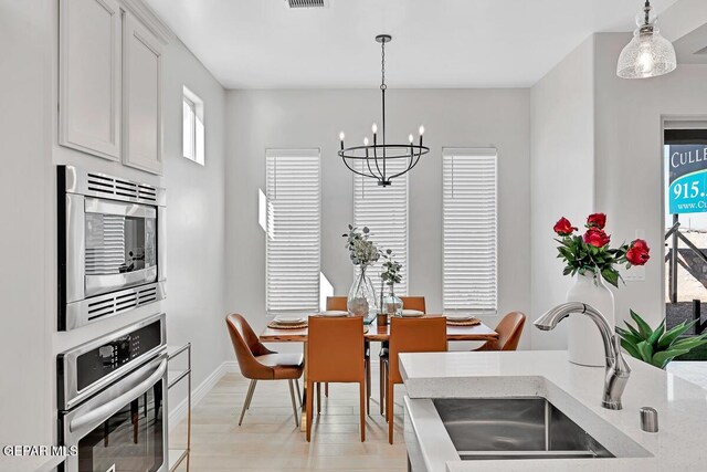 dining area with light wood-type flooring, sink, and a chandelier